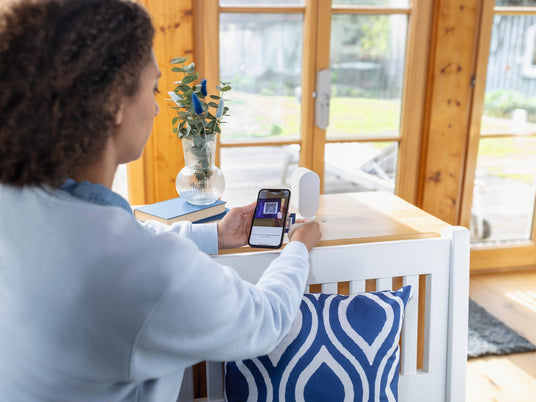 Frau bedient die ABUS One App, auf dem Tisch steht die ABUS BRIDGE One